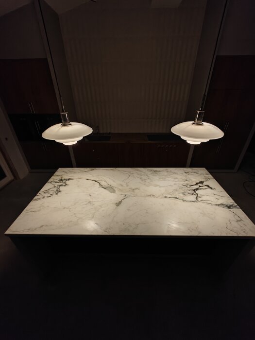 Marmorbord med mörka kanter under två vita hängande lampor i ett mörkt rum.