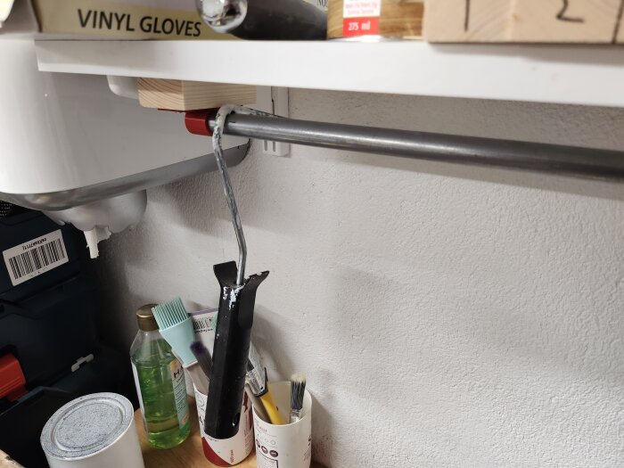 Vattenflöde genom rör, läckande PVC-genomföring, arbetsområde, vinylhandskar, hylla, färgflaska, redskap.