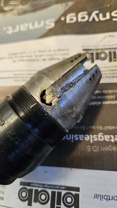Svart borrchuck skadad, metallspån, på tidning. Slitage eller olycka. Tekniskt verktyg, arbetsrelaterat. Fokus på skador.