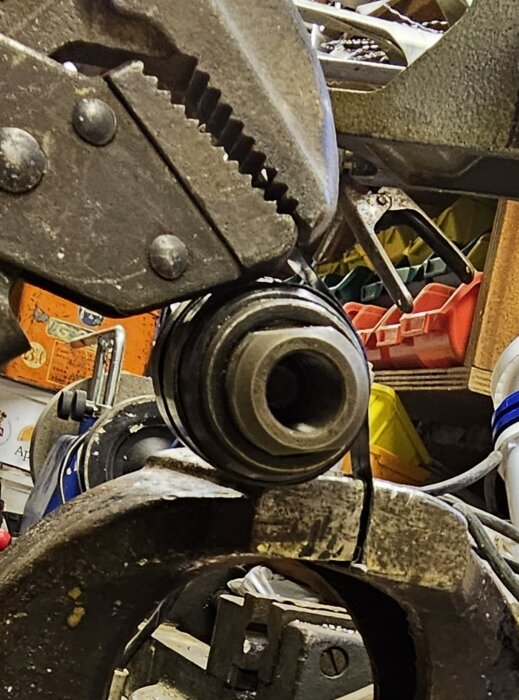 Verktyg i förgrunden, rörigt garage med diverse föremål i bakgrunden.