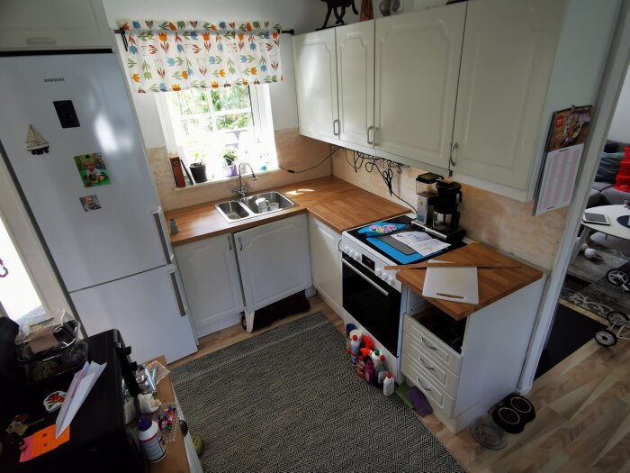 Ett modernt kök med kylskåp, spis, skåp och ett fönster med gardiner. Lekfull inredning, vardagliga köksartiklar synliga.