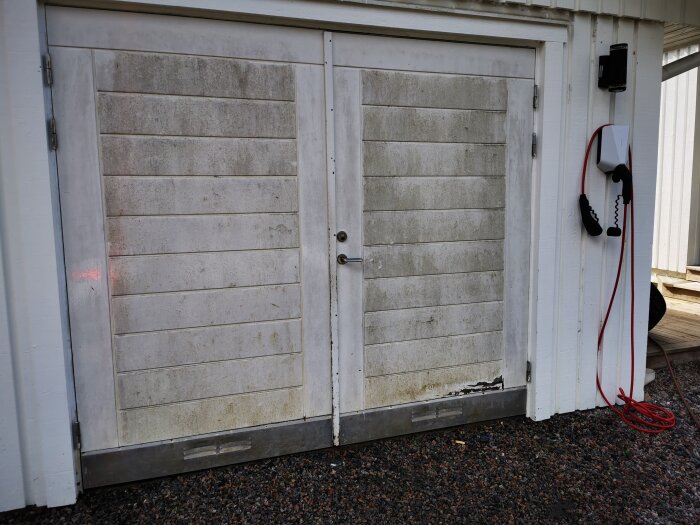 Gamla garageportar med smutsfläckar, telefon och grusig mark.