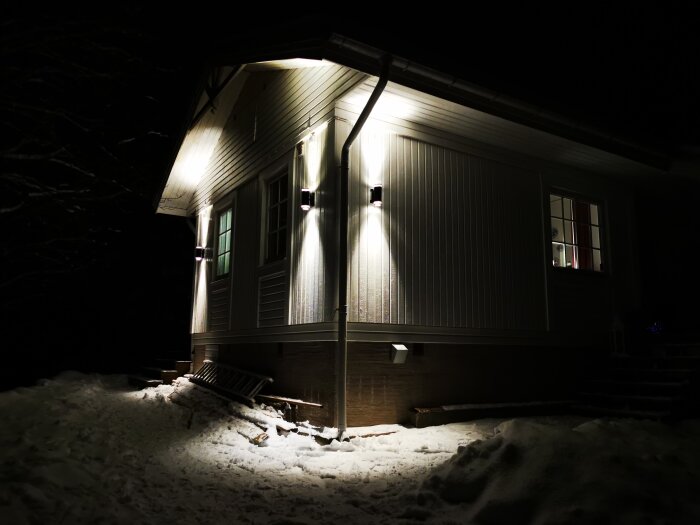 Ett upplyst hus om natten omgivet av snö med synlig mörk himmel och träd.