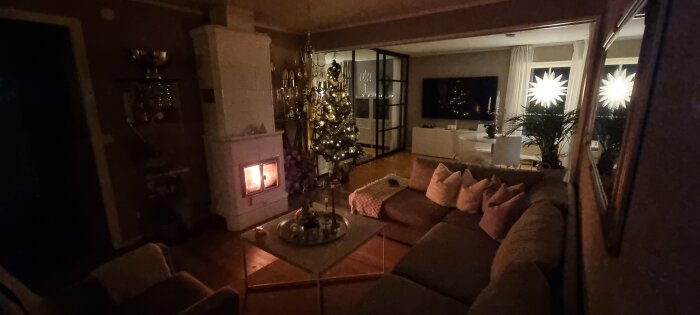 Mysigt vardagsrum, öppen spis, julgran, varmt ljus, hemtrevligt, adventsstjärnor i fönster, mörkt ute.
