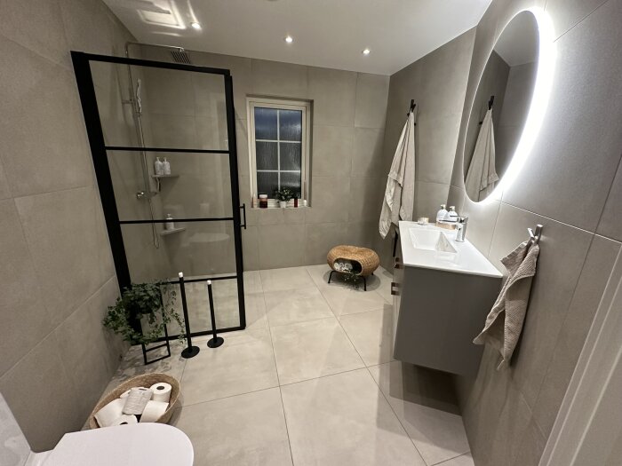 Modernt badrum med duschkabin, spegel, handfat, toalett, handdukar och gråa toner.