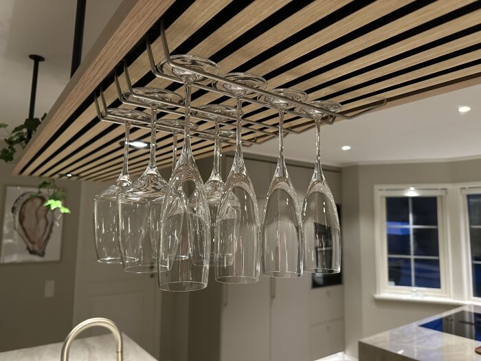 Vin- och champagneglas hängandes upp och ner på ett glashållare över en köksö. Modernt kök i bakgrunden.