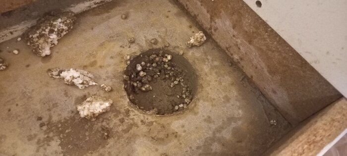 Nedsmutsad yta med hål omgivet av fragment, möjligen gammal rörinstallation eller sanitär utrustning.