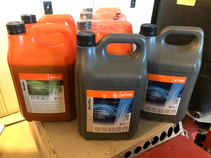 Fem genomskinliga jerrycan-dunkar med etiketter, två orange, tre grå, på golv.