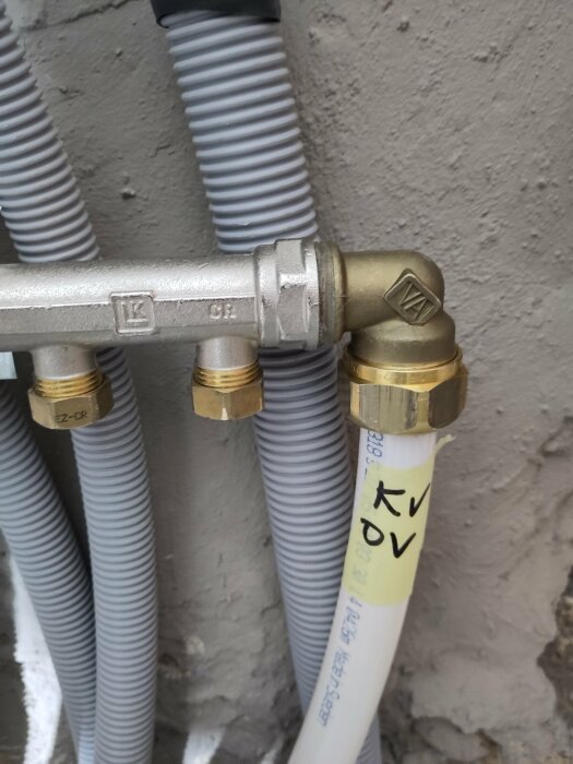 Metall och plast VVS-röranslutningar, ventiler och märkningar mot en betongvägg.