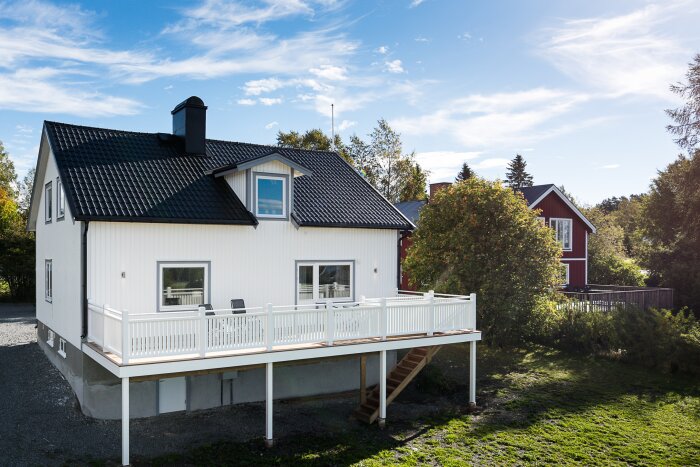 Vitt hus med svart tak, altan, grönt gräs och klart himmel.