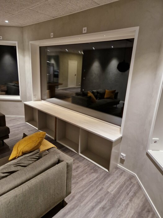 Modernt inrett rum med spegel, soffa, kuddar, och inbyggd hylla. Lugna färger och stilren design.