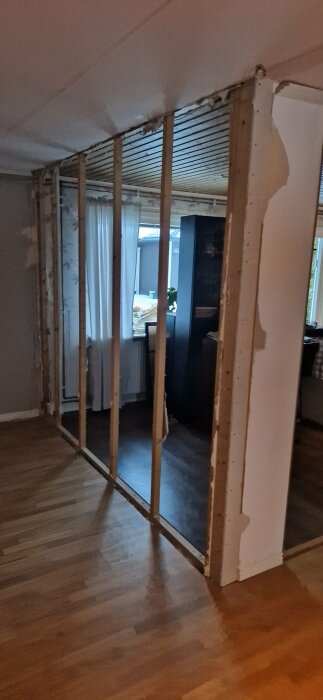 Inre renovering, träreglar utan väggskivor, synliga kablar, byggarbete pågår, inomhus, bostadsutrymme, öppet till annat rum.