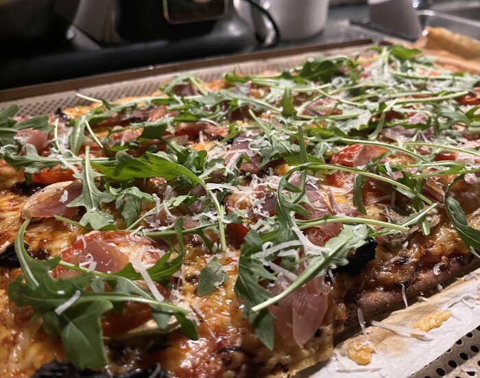 Nygräddad pizza med tomater, ruccola och parmaskinka på ett bakplåtspapper.