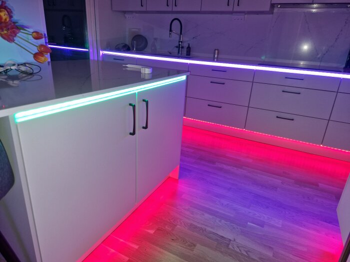 Modernt kök med vita skåp och LED-belysning i blått, lila och rött under skåpen och på golvet.