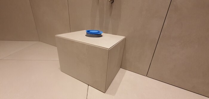 Brun kubformad låda i ett hörn med en blå locket på toppen, minimalistiskt och enkelt.