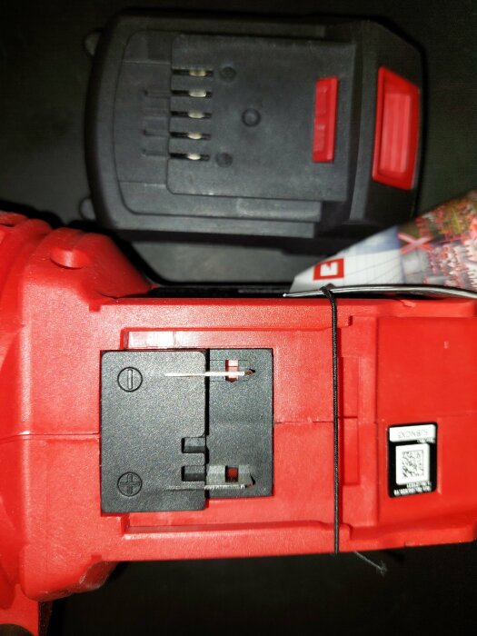 Röd elverktygsbatteri och laddare, närbild, svart plast, QR-kod, terminaler klara för anslutning.