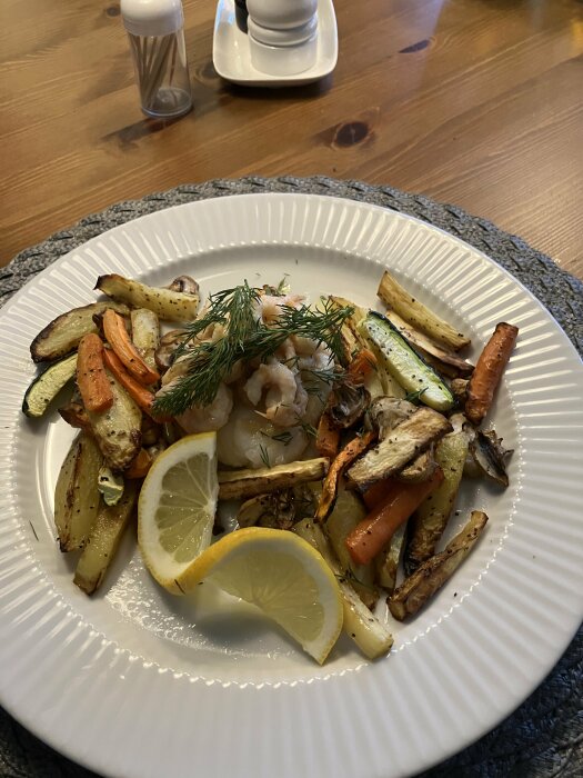 Rostade rotfrukter och grönsaker med räkor på vit tallrik, citronskivor, dill, salt- och pepparkar i bakgrund.