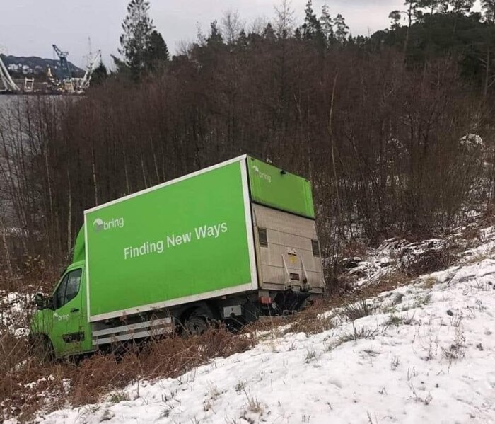 Lastbil med texten "Finding New Ways" fastnat i terrängen på en snötäckt sluttning, ironisk situation.