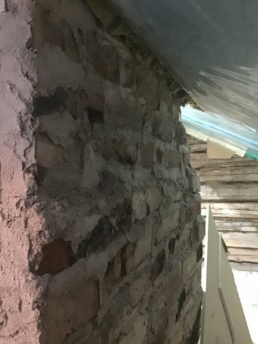 Tegelvägg under konstruktion eller renovering, med synliga murbruk och ojämnt lagda tegelstenar.