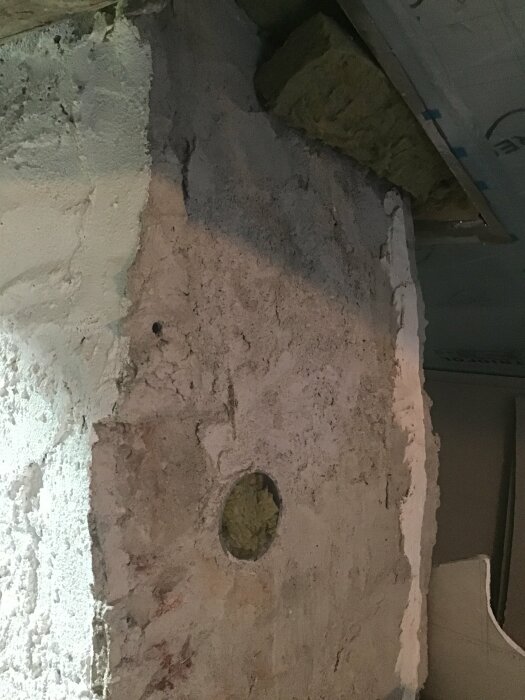 Ofärdigt hörn med exponerad isolering och genomföringshål i en betongvägg. Byggarbete verkar pågå.