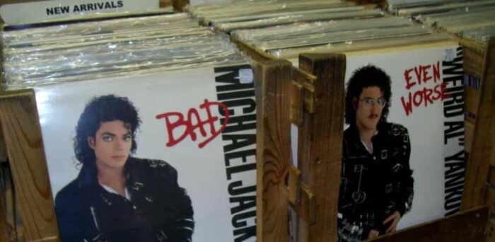 Skivbutik, två albumomslag, humoristisk jämförelse mellan konstnärernas stil och uttryck. Vinylskivor, trähylla, nyheter.