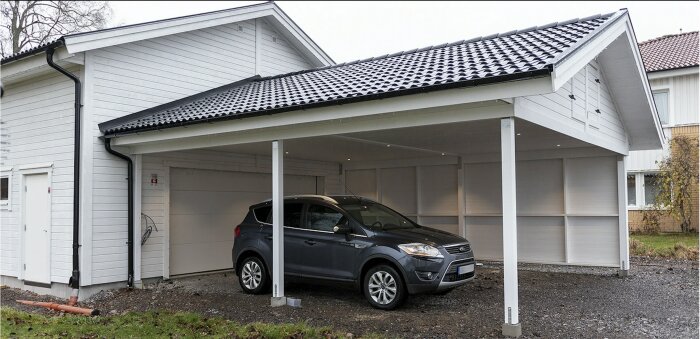 Carport vid vitt hus, grå bil parkerad, molnig dag, minimalistisk design, bostadsområde.