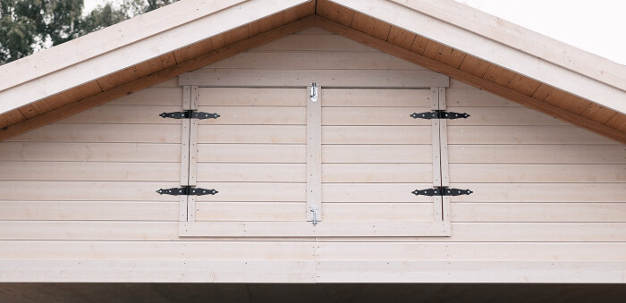 Träfasad, symmetriskt fönsterluckor, husknut, enkelt och minimalistiskt, svarta gångjärn och lås.