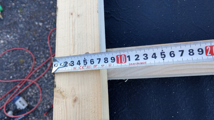 Måttband på trä, mäter cirka 62 centimeter, byggarbetsplats, utomhus, dagsljus, närbild.