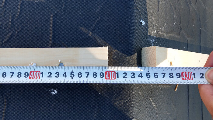 Meterstock måler et trestykke på svart stoffunderlag utendørs. Cirka 41 centimeter synlig. Lyst tre, måleverktøy i fokus.