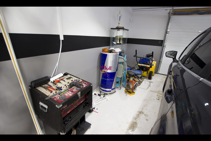 Garage med bil, Red Bull-kyl, verktyg, troféskåp och RC-bil. Svart-vit vägg. Oorganiserad inredning.