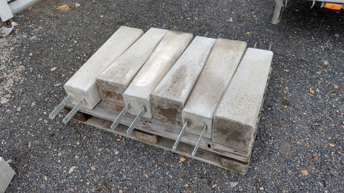 Betongplintar staplade på en pall, konstruktionsmaterial för anläggningsarbete, utomhus på grusunderlag.