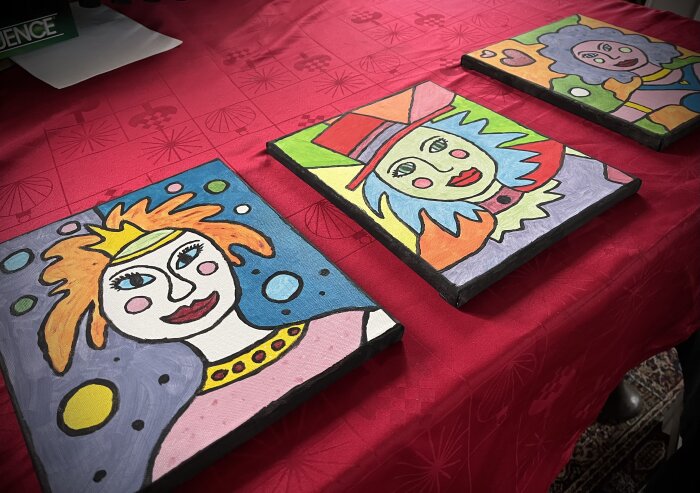 Tre målade clownporträtt på duk, färgglada, abstrakt stil, röd duk med mönster, informellt konstuttryck.