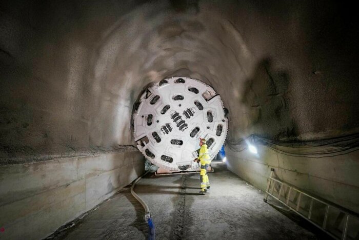 Arbetare står bredvid enorm tunnelborrmaskin i en nyligen uthuggen tunnel.