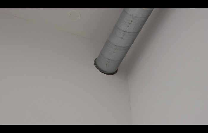 Ett ventilationsrör i taket, vita väggar, sparsam inredning, modern stil.