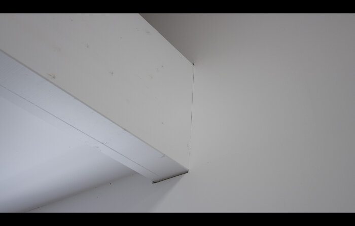 Vit vägg och tak möts vid en hörn med synliga smutsfläckar och nötning.