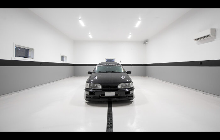 Svart sportbil parkerad centralt i en vit, ren garageinteriör med lysande taklampor.