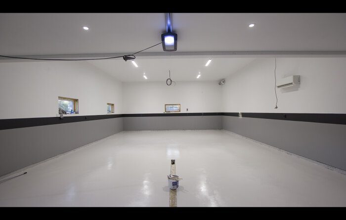 Tom lokal med vitmålade väggar och golv, spotlights i taket, speglar på väggen och en färgburk i mitten.