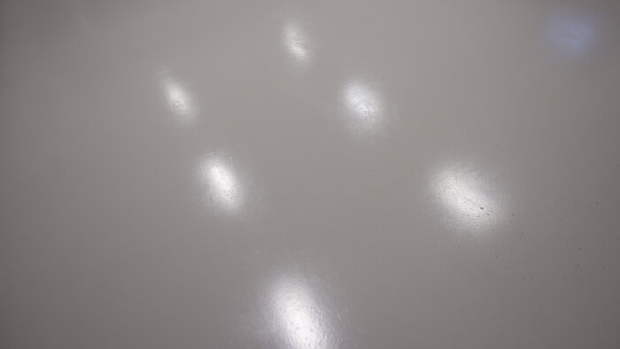 Glansig yta med reflekterande ljuspunkter. Minimalistisk, ren, ljus, gråtonad textur.