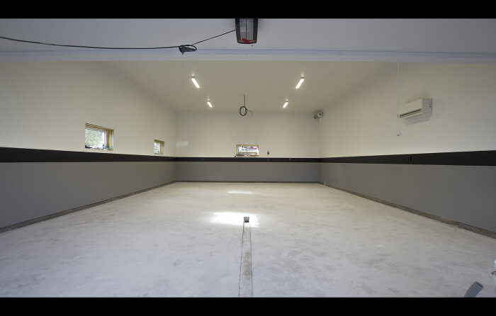 Tom, nyrenoverad garageinteriör med belysning, luftkonditionering, fönster och betonggolv.
