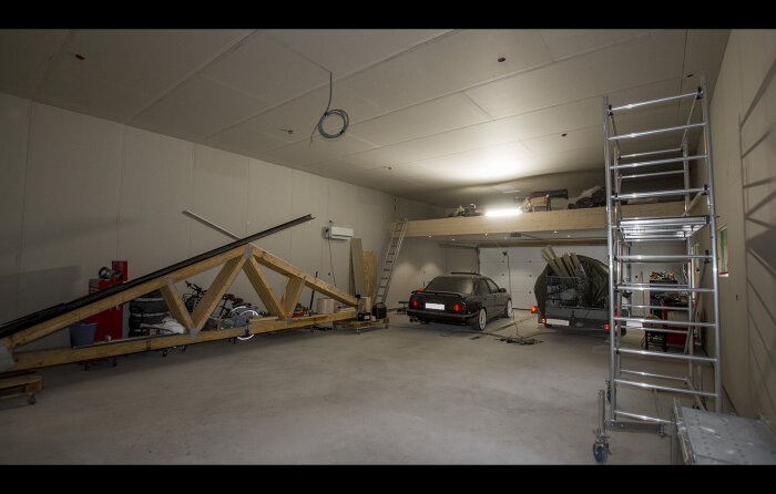 Garage med bil, utrustning, stege, halvfärdigt loft, belysning, verktyg, konstruktion, byggprojekt under arbete.