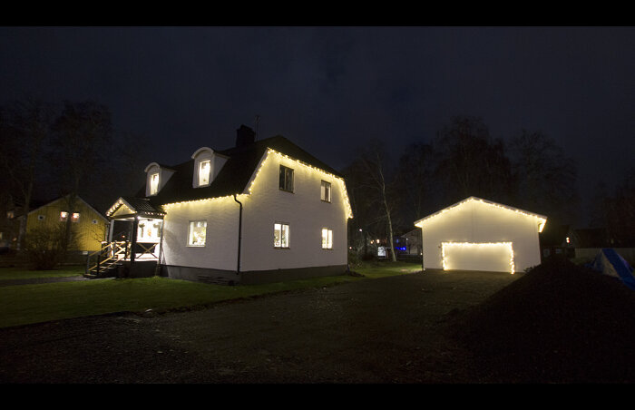 Vit hus med julbelysning, garage i mörk kväll, stillsam atmosfär.