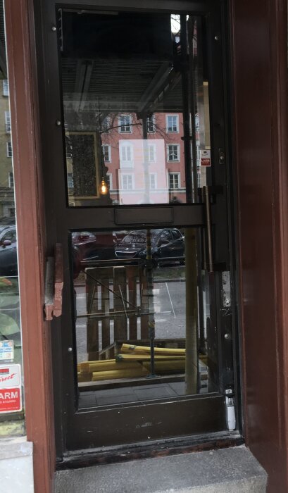 Glassdörr till en lokal, reflektion av byggnader och en bil, inuti syns stolar och ett bord.