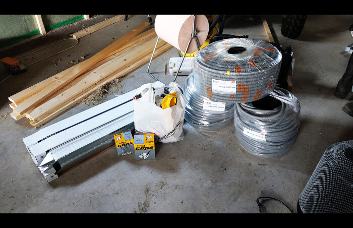 Byggmaterial och verktyg i en garageverkstad: trä, kablar, skydd och belysning.