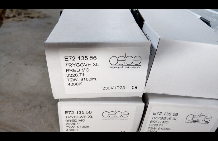 Staplar med vita kartonger märkta "TRYGGVE XL", produktspecifikationer och "cebe" logotyp, antagligen elektronik- eller ljusprodukter.