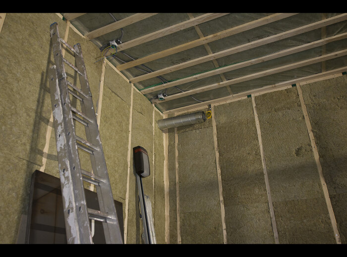 Byggarbetsplats-inredning med stegar, isolering, träreglar och ventilationsrör. Under konstruktion eller renovering.