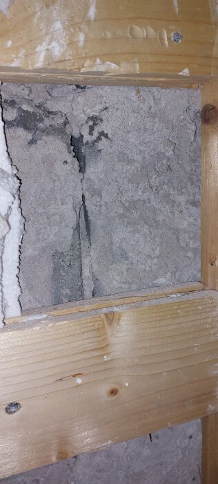 Sprucken betongvägg med träram och isoleringsskum vid en byggnadsplats. Strukturella skador synliga.