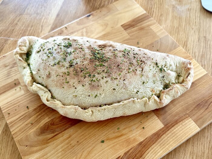 En stor, nylagad calzone med örter på en träskärbräda.