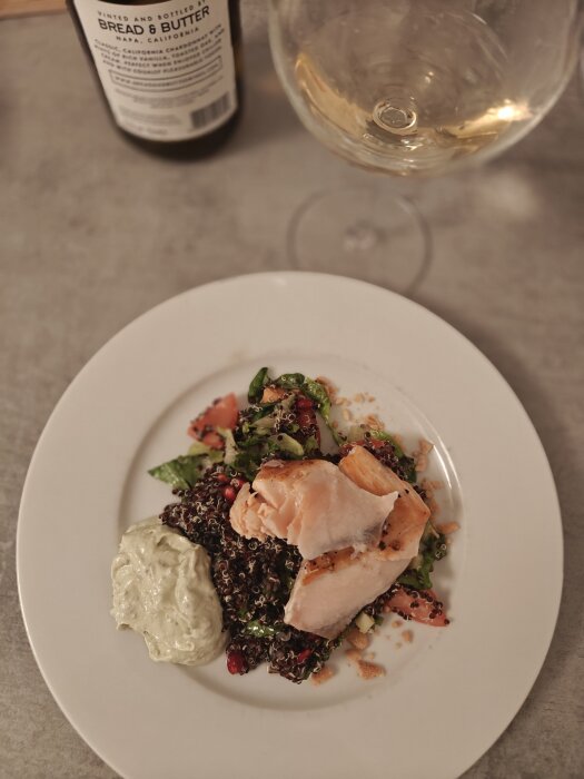 Laxfilé på en sallad med quinoa, vinflaska och ett glas i bakgrunden.