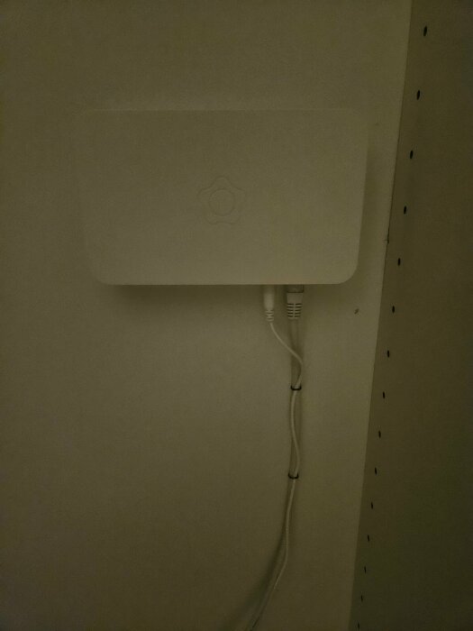 En vit väggenhet med kablar kopplade till den, möjligen en router eller modem, intill en perforerad platta.