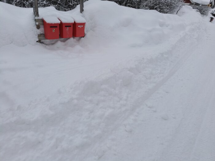 Vinterlandskap med djup snö, röda brevlådor, snöig väg och spår av aktivitet.